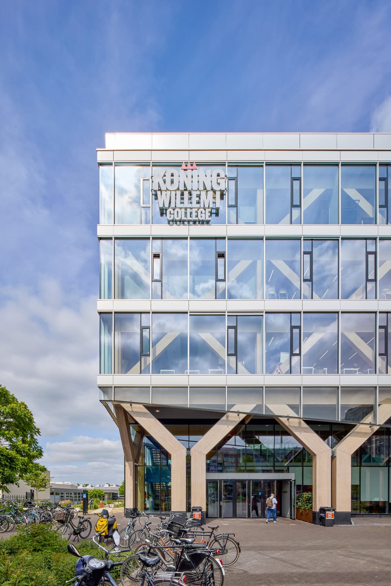 Voorgevel Koning Willem I College met glazen gevel en houten constructie, gezien vanaf de straatzijde.