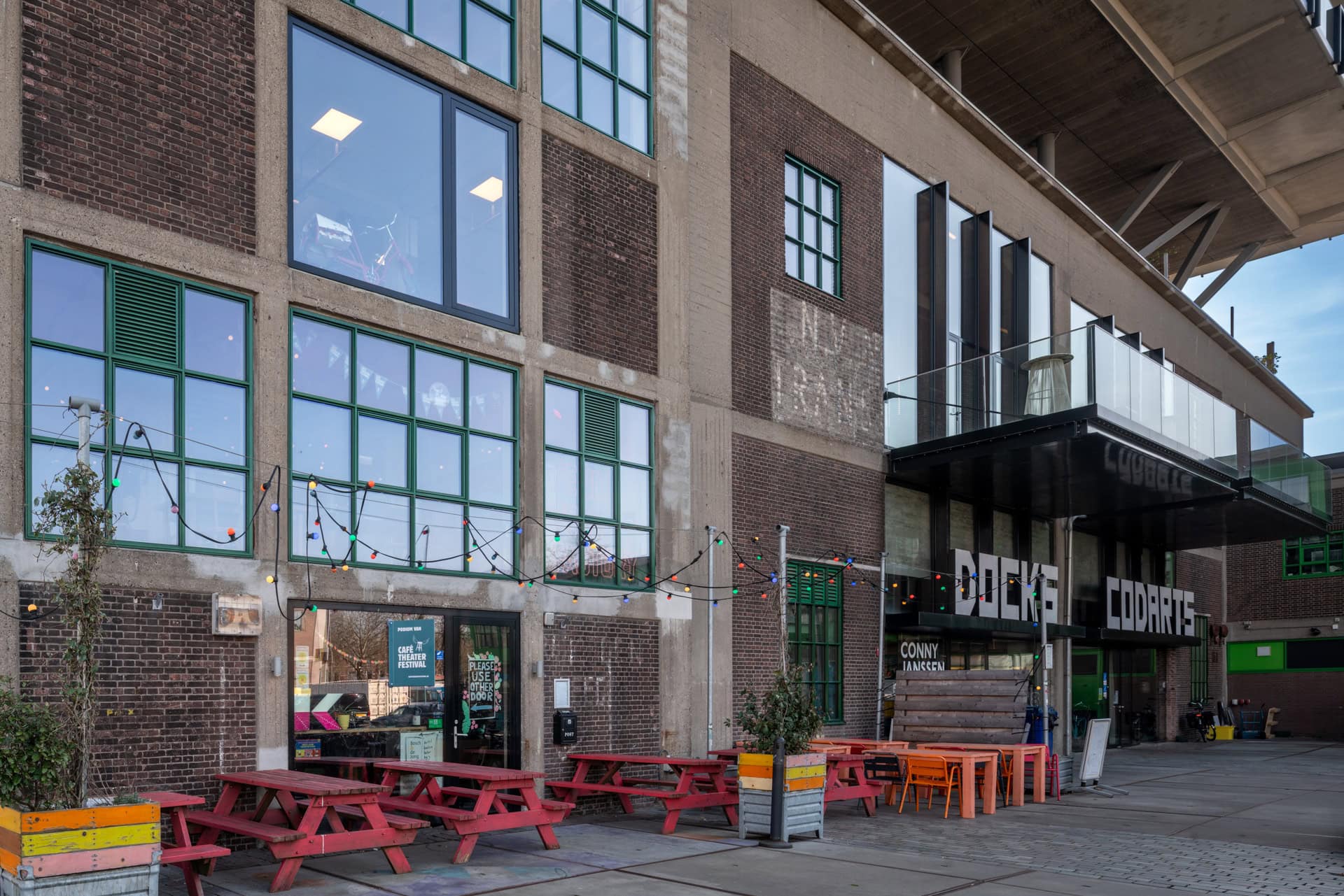 Industrieel gebouw met grote ramen van floatglas (geïsoleerd), kleurrijke picknicktafels en een overdekte ingang.