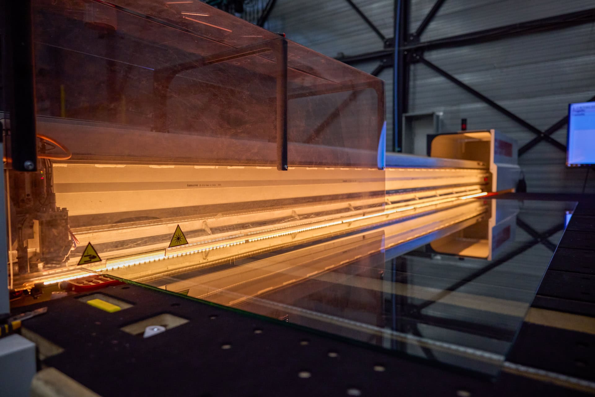 Een industriële machine verwerkt een groot stuk floatglas in een fabriekshal.