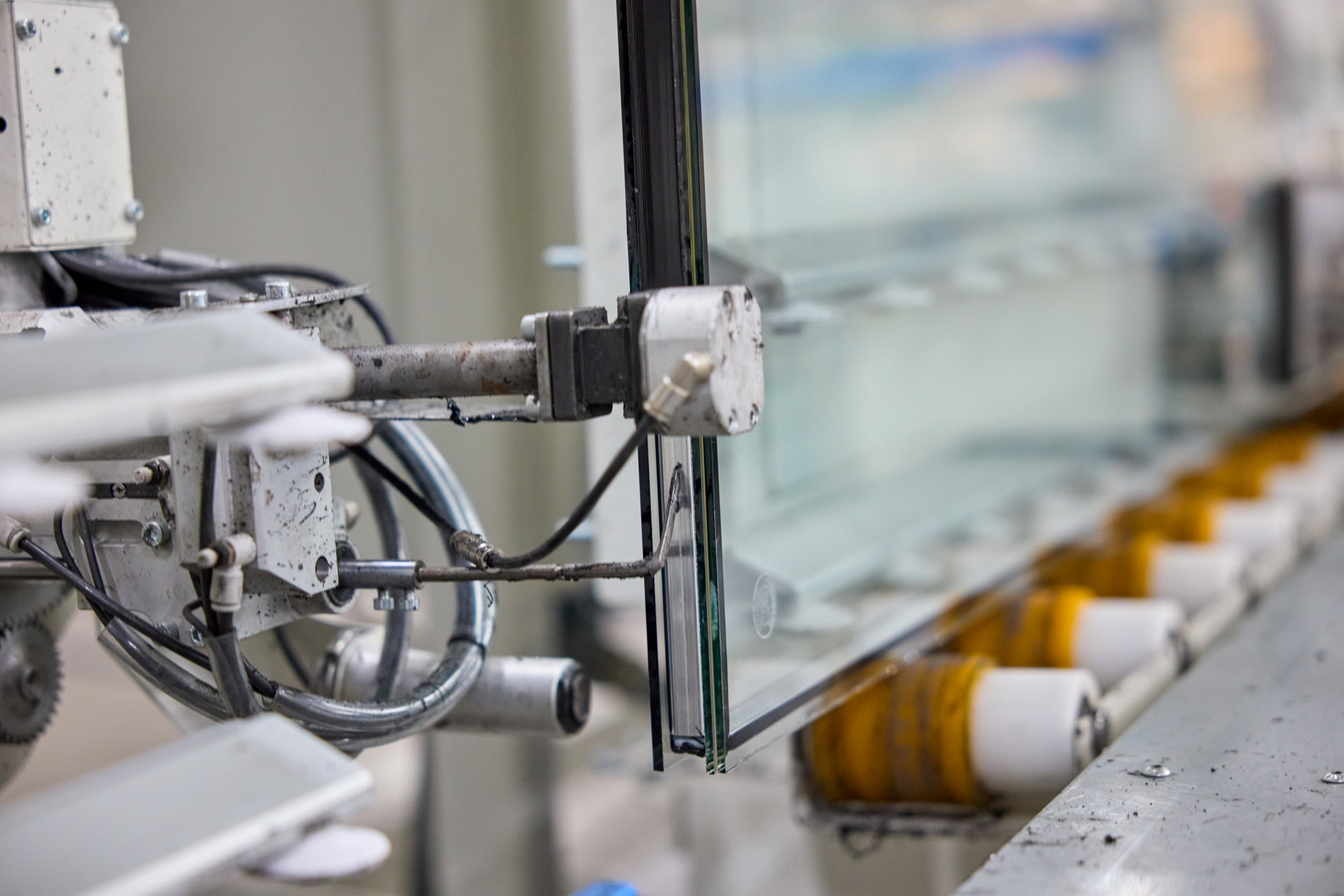 Een close-up van een industriële machine van Mosa Glas die glasplaten verwerkt. De machine heeft metalen armen en grijpers die de glasplaten vasthouden en dicht sealt. 