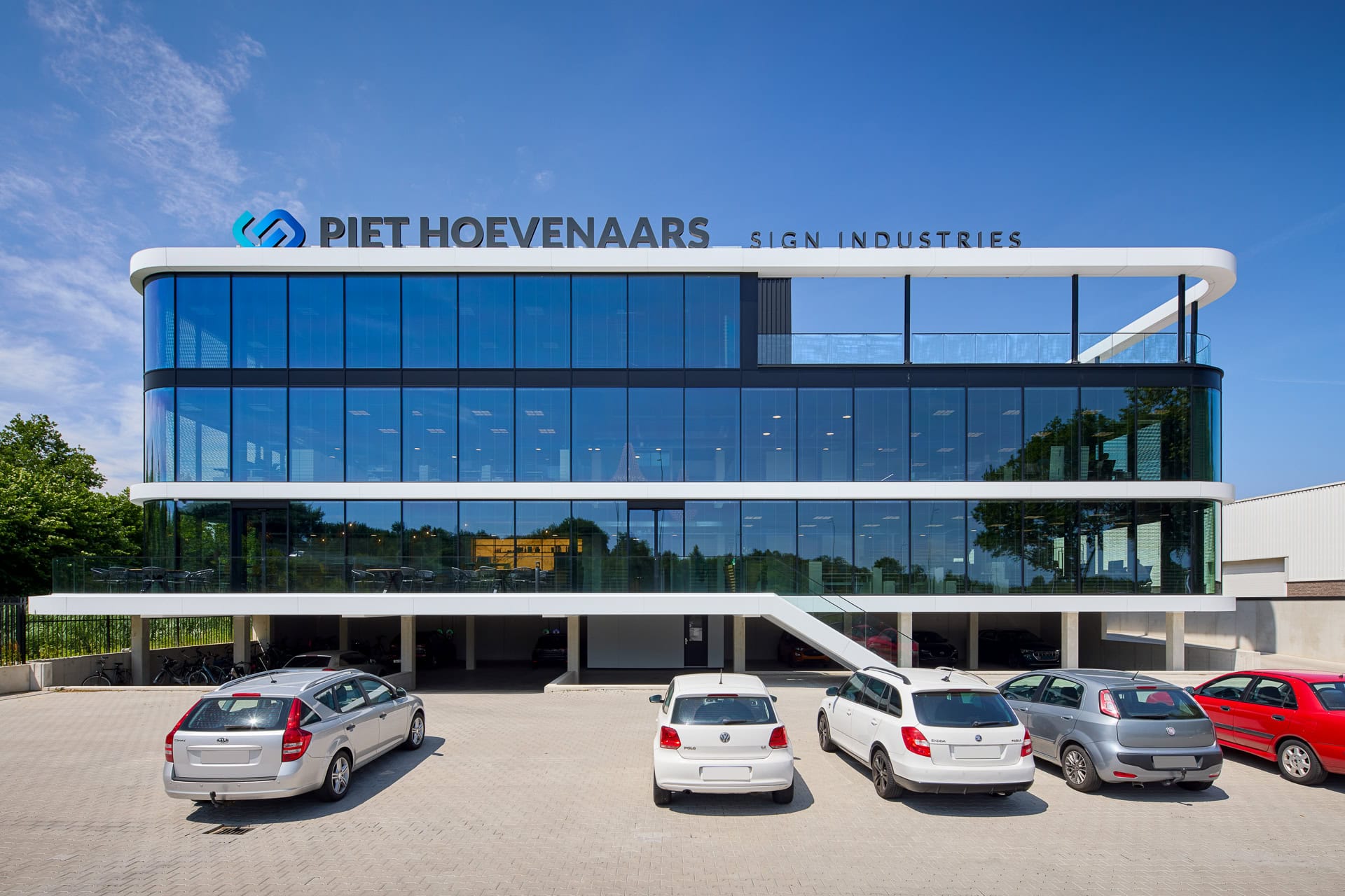 Modern kantoorgebouw van Piet Hoevenaars Sign Industries met glazen gevel en parkeerplaats op de voorgrond.