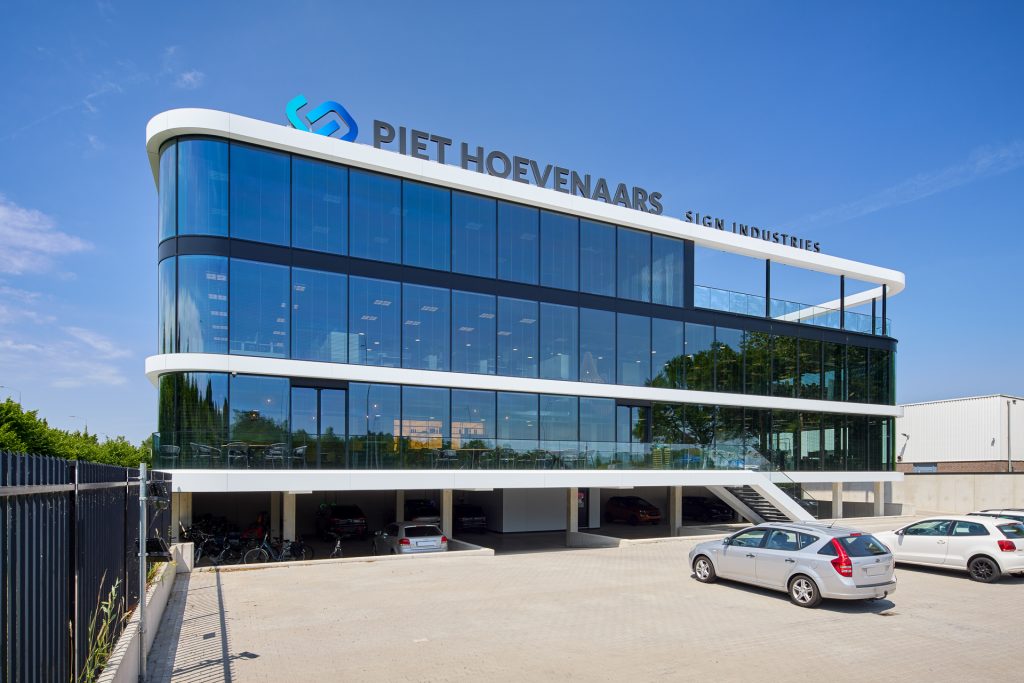 Modern kantoorgebouw van Piet Hoevenaars Sign Industries met glazen gevel en parkeerruimte.