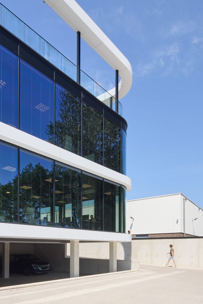 Modern gebouw met grote glazen ramen, open garage en een persoon op het trottoir.