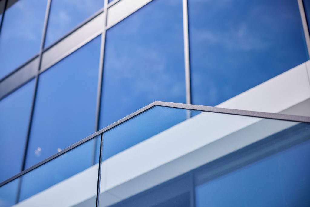 Moderne gevel met blauwgetinte glazen ramen en glazen balustrade op de voorgrond.